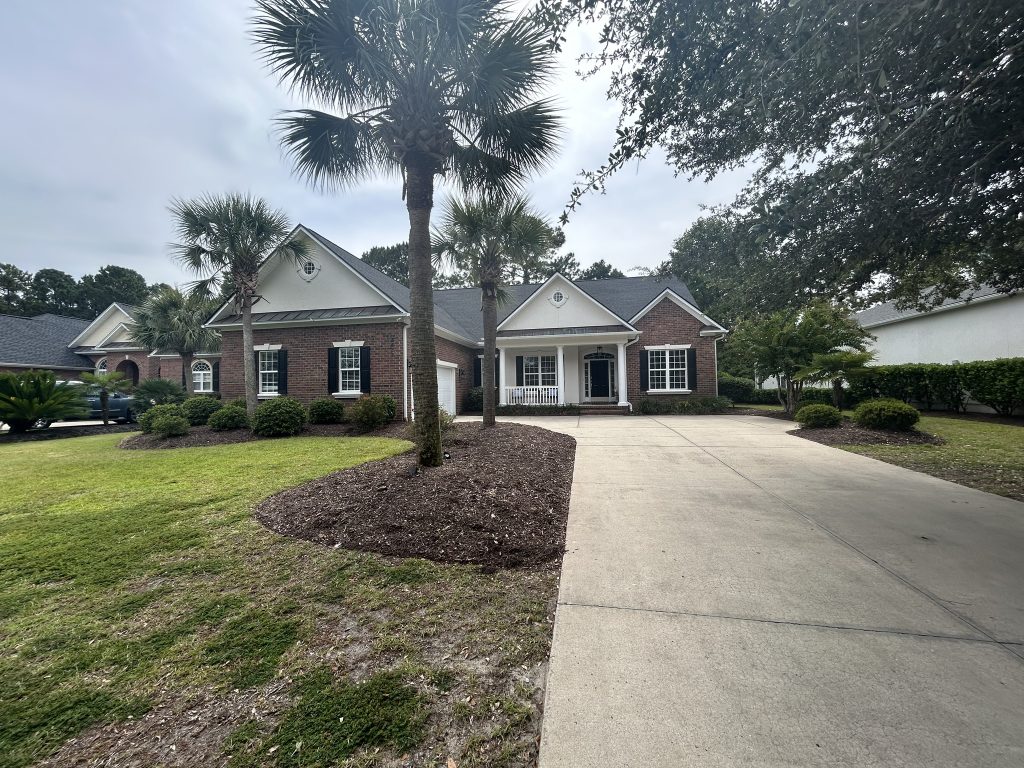Two-story home with dark shingle roof viewed from a palm-tree-lined driveway in Myrtle Beach, SC