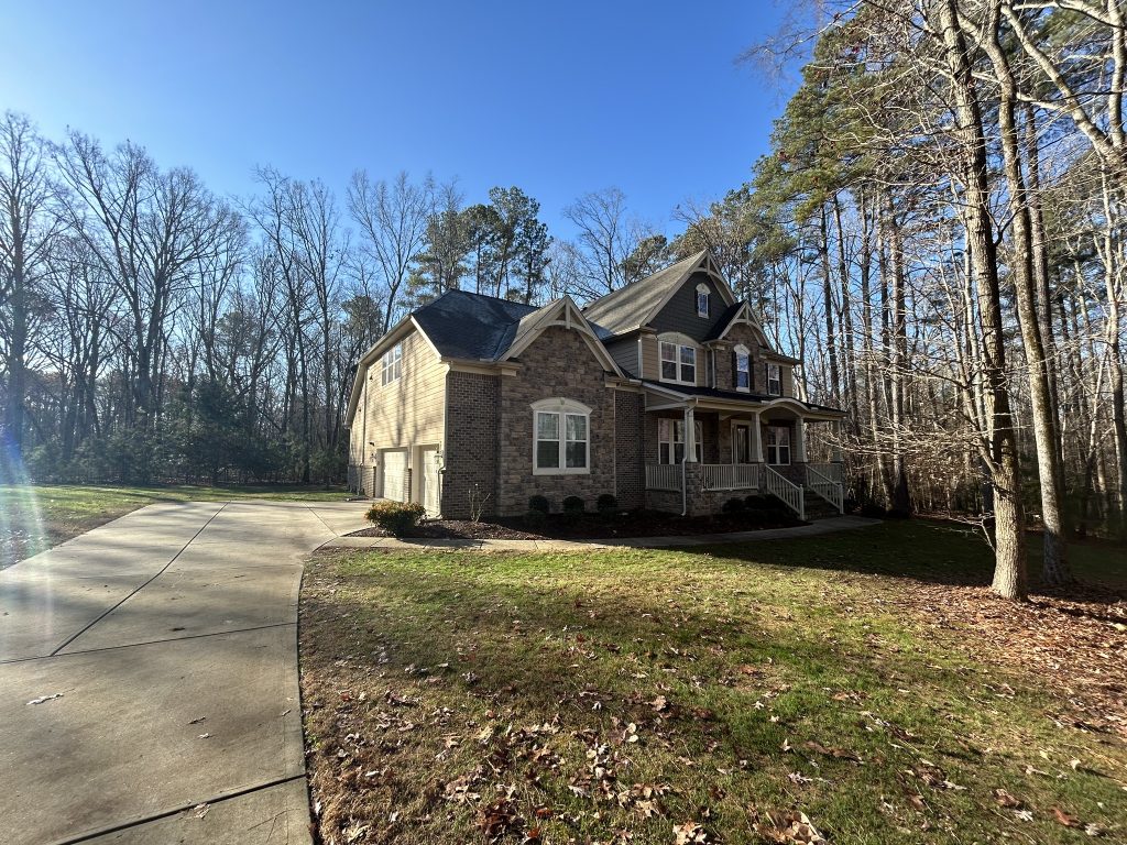 Two-story home with a covered porch and new dark shingle roof in Raleigh, NC