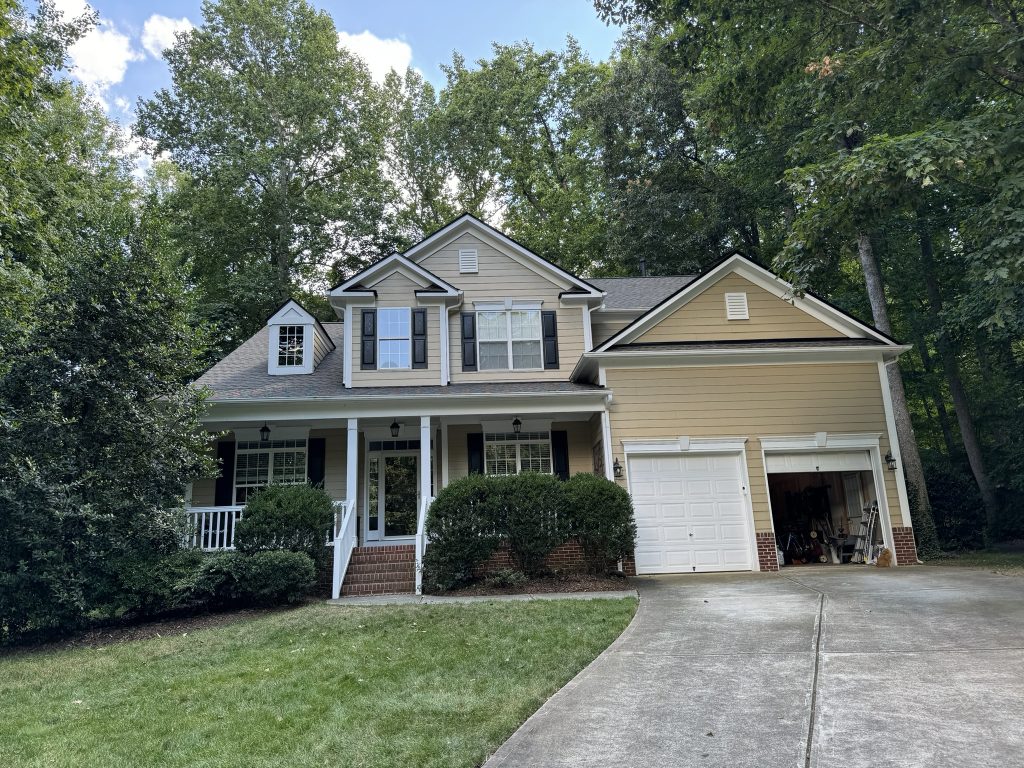 Two-story brick home with a newly installed dark shingle roof in a wooded neighborhood in Raleigh, NC