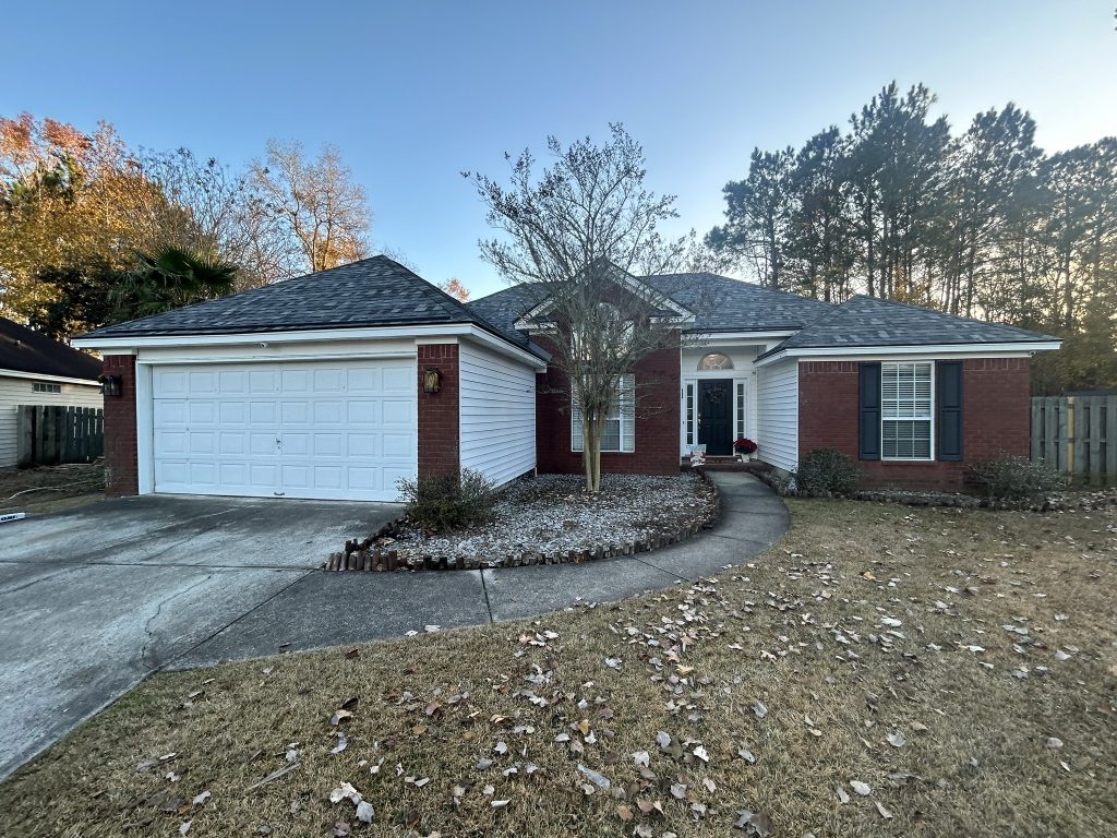 Brick and white ranch home with a new dark shingle roof surrounded by autumn trees in Savannah, GA