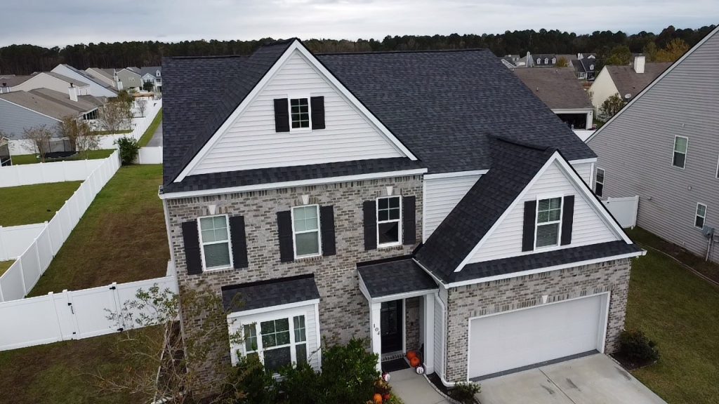 Two-story tan home with a covered front porch and new dark shingle roof in Savannah, GA